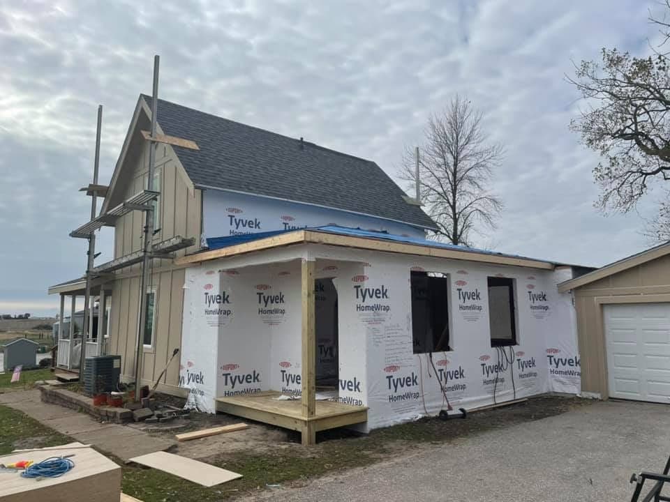 A single-storey addition going up on an older house, wrapped in housewrap with the new roof on and the porch posts framed.