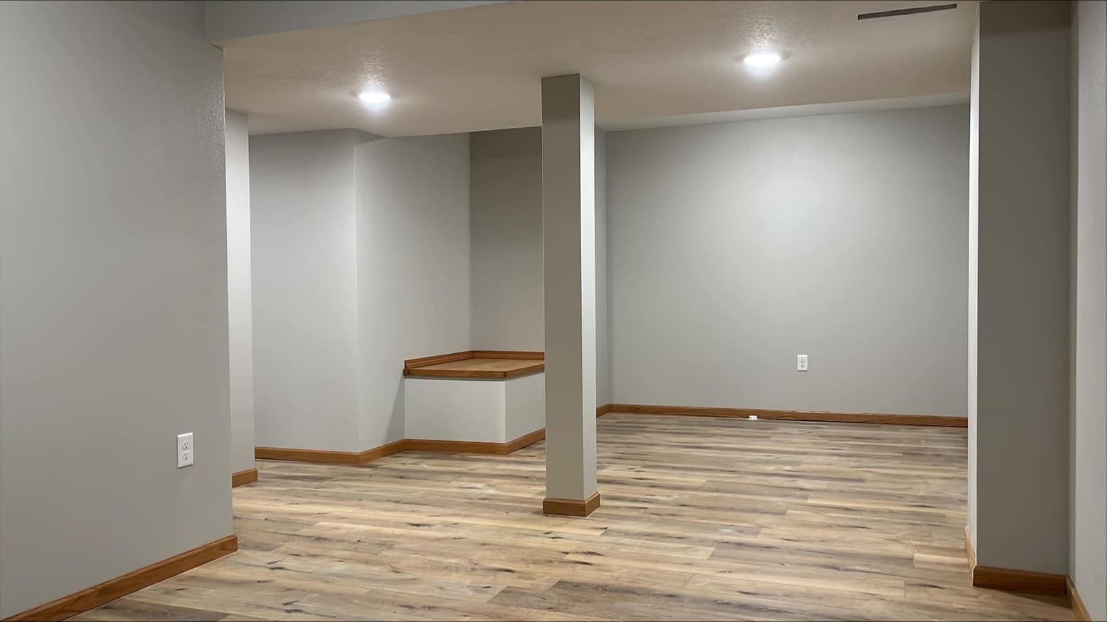 A finished basement with recessed lighting, a wrapped structural post and plank flooring through it.