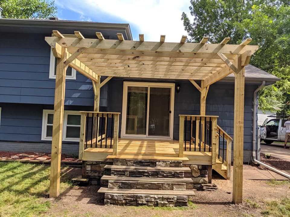 A pergola over a new deck at the back of a blue house