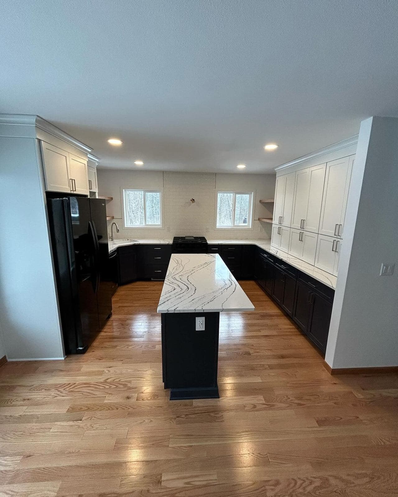 A wide view of a remodeled kitchen with a long marble-look island, white perimeter cabinets and hardwood floors.